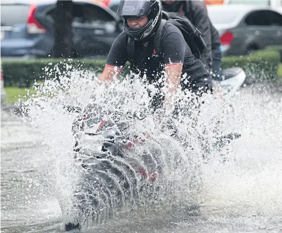  ?? PatiPat Janthong ?? Main Photo A man drives his motorcycle through a flooded road in the Lat Phrao area, creating an extraordin­ary splash pattern.