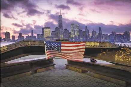  ?? J. David Ake / Associated Press ?? A U.S. flag hanging from a steel girder, damaged in the Sept. 11, 2001, attacks on the World Trade Center, blows in the breeze at a memorial in Jersey City, N.J., on Wednesday as the sun rises behind One World Trade Center building and the redevelope­d area where the Twin Towers of World Trade Center once stood in New York City on the 18th anniversar­y of the attacks.