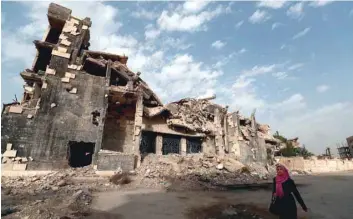  ?? — AFP ?? A woman walks past a damaged building in the Syrian city of Raqa on Saturday.