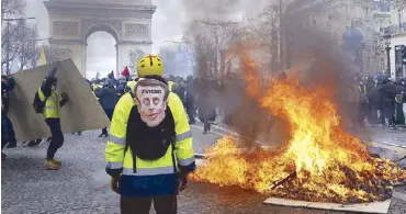  ?? REUTERS ?? A protester carrying a bag with a drawing depicting French President Emmanuel Macron stands near a burning barricade during a yellow vest demonstrat­ion on ChampsElys­ees Avenue in Paris on Saturday.