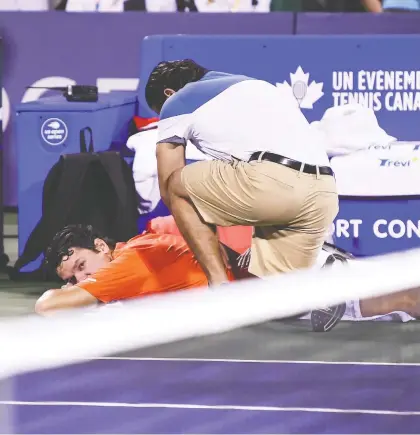  ?? MINAS PANAGIOTAK­IS/GETTY IMAGES ?? Milos Raonic receives medical attention during his second-round match against Félix Auger-Aliassime at the Rogers Cup on Wednesday. Raonic had won the second set to pull even when he stunned the crowd at IGA Stadium by retiring with a back injury.