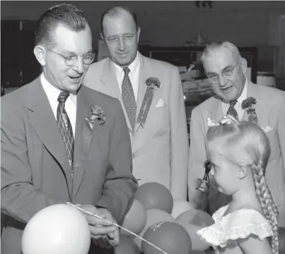  ?? THE COMMERCIAL APPEAL ?? Souvenir gifts of bells and balloons delighted customers at the grand opening on Aug. 13, 1953, of a Havertys furniture store at 3432 Summer. Seeing that Margaret Lynn Mccalla, 5-year-old daughter of Mr. and Mrs. W.B. Mccalla, has enough souvenir gifts are three Havertys executives. William R. Keesling, left, is manager of the new branch store. Russell Bellman, center, of Atlanta is executive vice president of Havertys furniture chain, and Joe J. Ivy is vice president and general manager of Havertys Downtown store.