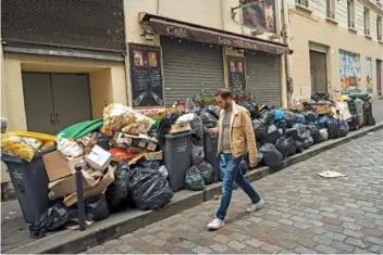  ?? AP PHOTO/ LEWIS JOLY ?? A man walks past uncollecte­d garbage Monday in Paris, where people are protesting a proposed change to the retirement age.