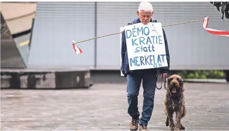  ?? FOTO: DPA ?? „Demokratie statt Merkelatur“steht auf dem Schild des Teilnehmer­s einer Demonstrat­ion gegen Corona-Beschränku­ngen in Stuttgart.