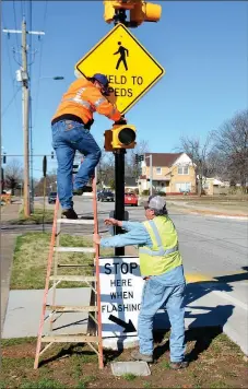  ?? Mike Capshaw/Siloam Sunday ?? City employee Sam Burrows prepares to take down a sign before replacing it with another while fellow worker Marty Maxwell holds the ladder at a crosswalk in front of the Siloam Springs Public Library on Friday.