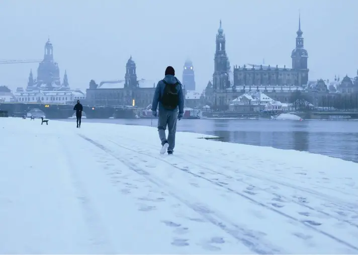  ??  ?? Passers-by walk through the snow in the morning on the banks of the Elbe river against the backdrop of the old town in Dresden, Germany, yesterday. Photo: AP