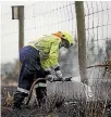  ??  ?? A firefighte­r douses a smoulderin­g fencepost after a grass fire swept through Hororata.
