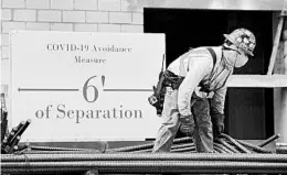  ?? WILFREDO LEE/AP ?? A constructi­on worker wears a protective mask in the pandemic as he unloads a truck.