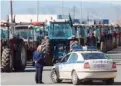  ??  ?? An officer stands next to a police car in front of parked tractors as farmers block the Athens-Thessaloni­ki highway at Nikaia.