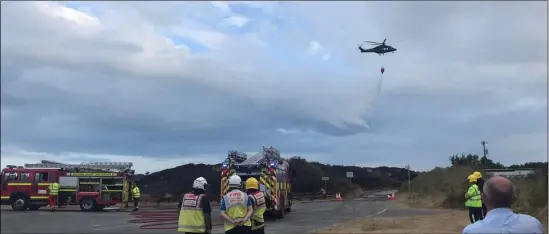  ??  ?? Top, left: A graphic showing the trail of the Air Corps helicopter as it battled the blaze; top, right: local farmers use slurry tanks to spray water on to the dunes; above: firefighte­rs look on as the Air Corps helicopter drops water on to the affected area.