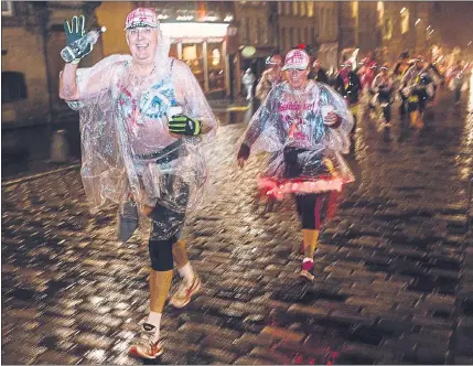  ??  ?? SMILING THROUGH: Two MoonWalker­s wear plastic ponchos as they brave the rain during the weekend charity event in Edinburgh. Picture: Guy Aubertin