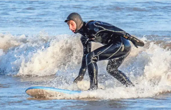  ?? KLEIN/SHEBOYGAN PRESS PHOTOS BY GARY C. ?? Dominic Flores, of Sheboygan, balances on his surfboard while catching a wave at the Sheboygan lakefront on December 16, in Sheboygan, Wis.