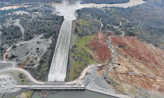  ?? Josh Edelson AFP/Getty Images ?? AN AERIAL PHOTO taken from behind the Oroville Dam shows 100,000 cubic feet of water being released each second down the facility’s main spillway on Monday. Interviews and records suggest that design problems with the emergency spillway, seen to the...