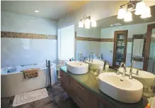  ??  ?? Vessel sinks, on a glass counter in the ensuite, echo the shape of the freestandi­ng tub. White ceramic tile on the wall, from Decora, has a brown accent line.