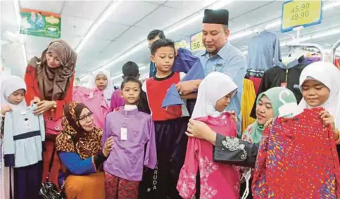  ?? PIC BY MOHD RAFI MAMAT ?? SK Padang Garuda Welfare club chairman and headmaster Mohd Al Hamadi Abu Bakar (standing, right) helping his pupils choose their Hari Raya Aidilfitri clothes in Kuantan yesterday.