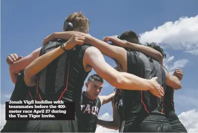  ??  ?? Jonah Vigil huddles with teammates before the 400meter race April 27 during the Taos Tiger Invite.