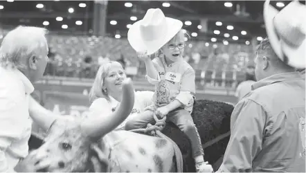  ?? Steve Gonzales / Houston Chronicle ?? Collins Bellow holds up her hat as she rides a wooden steer during the Houston Livestock Show and Rodeo Lil' Rustlers event for kids with special needs on Tuesday. The program welcomed 57 kids ages 4 to 10 to the rodeo experience.