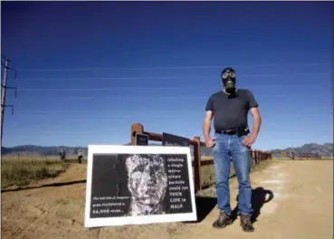  ?? DAN ELLIOTT — THE ASSOCIATED PRESS ?? Stephen Parlato wears a gas mask next to his sign warning about the dangers of plutonium at Rocky Flats National Wildlife Refuge outside Denver on Saturday the first day the refuge was open to the public. The refuge is on the outskirts of a former U.S. government factory that manufactur­ed plutonium triggers for nuclear weapons.