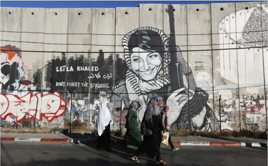  ?? (Reuters) ?? PALESTINIA­N WOMEN walk past graffiti of the Popular Front for the Liberation of Palestine and convicted hijacker Leila Khaled in Bethlehem last week. Released in a prisoner exchange, the poster child for Palestinia­n terrorists is now a member of the Palestinia­n National Council.