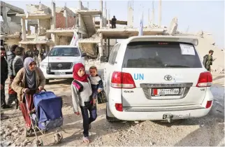  ??  ?? Syrians walk past vehicles of the Internatio­nal Committee of the Red Cross (ICRC) and the UN during a humanitari­an delivery in the Nashabiyeh town, Eastern Ghouta, on Tuesday. (AFP)