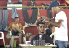  ?? PHOTO/ERALDO PERES ?? In this March 8 photo, Venezuelan Leonardo Wilfredo cuts a client’s hair at his makeshift barbershop inside a migrant shelter at the Tancredo Neves Gymnasium in Boa Vista, Roraima state, Brazil. Police say Venezuelan­s are sometimes working for as...