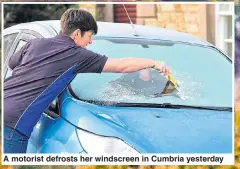  ??  ?? A motorist defrosts her windscreen in Cumbria yesterday