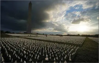  ??  ?? Clouds darken the Washington Monument on Friday as people walk among white flags that are part of artist Suzanne Brennan Firstenber­g’s temporary art installati­on, “In America: Remember,” on the National Mall. The installati­on consists of more than 630,000 flags in remembranc­e of Americans who have died as a result of covid-19.