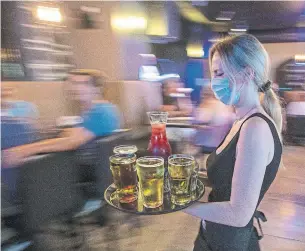  ?? LARS HAGBERG THE CANADIAN PRESS FILE PHOTO ?? A waitress delivers drinks inside the Blu Martini restaurant in Kingston. Ontario is expected to set out a road map this week for lifting capacity limits on venues like gyms, restaurant­s and bars.
