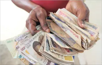 ??  ?? A petrol station attendant displays a large bundle of naira banknotes in Port Harcourt, Nigeria. The currency has lost 35 percent of its value in the past three months on the official exchange rate, yet has fared worse on the black market.