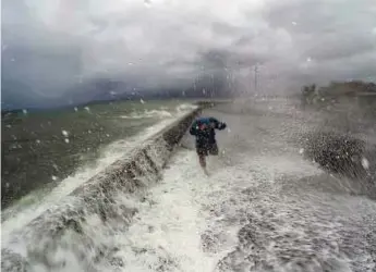  ?? AFP ?? Wave of trouble A resident dashes past waves spilling over a wall onto a coastal road in the city of Legaspi, Albay province, south of Manila yesterday as typhoon Melor approaches the city.