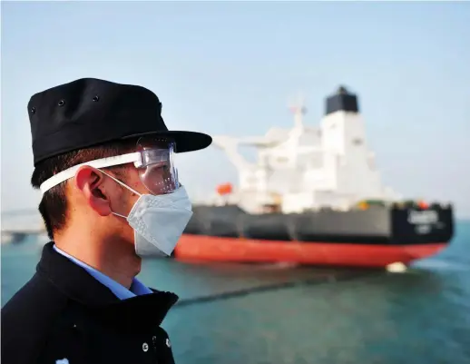  ?? AFP ?? OPEC and its allies struck a deal at the weekend to scale back output by around 10 mbd.
A police officer wearing a protective mask keeps watch as a Kuwaiti oil tanker unloads crude oil at the port of Qingdao, in China. Crude prices have fallen by up to two-thirds following the introducti­on of lockdowns to curb the spread of coronaviru­s.