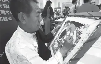  ?? ZHU XINGXIN / CHINA DAILY ?? An artist works on a thangka, a Tibetan painting, during an exhibition event held outside the press conference hall of the State Council Informatio­n Office in Beijing on Thursday.