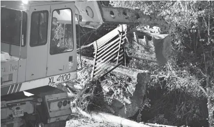  ?? KENNETH K. LAM/BALTIMORE SUN ?? A constructi­on worker uses heavy equipment to remove part of a fence and retaining wall holding up the sidewalk on East 26th Street.