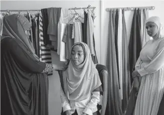  ??  ?? Sekina Abam, left, fits a hijab for a customer at her workshop in Accra, Ghana.