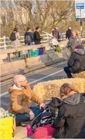  ??  ?? Rise and whine: Morning sees the camp of protesters awake in a makeshift hay field, while commuters make their way across the the bridge on foot