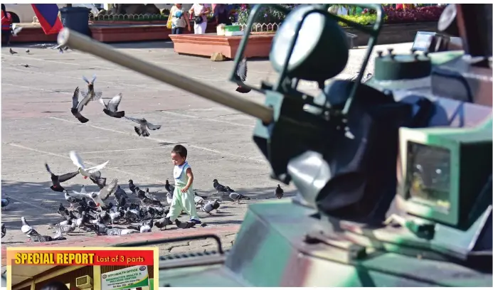  ?? MACKY LIM ?? SYMBOLS. A toddler enjoys the morning sun chasing pigeons at the Rizal Park while at the foreground is the armed personnel carrier of the Task Force Davao. The symbols of peace, the future, and conflict all in one.