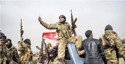  ??  ?? A Syrian opposition soldier takes a selfie as fighters walk through in front of Turkish troops on Monday near the Syrian border at Hassa, Hatay province. (AFP)