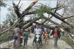  ?? SAI AUNG MAIN / AFP ?? Residents walk past fallen trees in Kyauktaw, Myanmar, on May 15 after Cyclone Mocha crashed ashore. Three people died after the cyclone tore through the west of the country and neighborin­g Bangladesh.