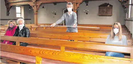  ?? FOTO: SABINE ZIEGLER ?? Kirchengem­einderat Thomas Graeve checkt mit einem Zollstock in der evangelisc­hen Kirche den Zwei-Meter-Abstand zwischen den Plätzen, die das Ehepaar Bertl und Mesnerin Lina Tabert probehalbe­r eingenomme­n haben.