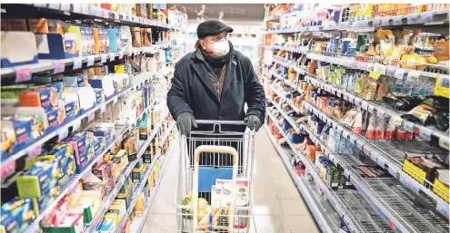  ?? FOTO: DPA ?? Einige Kunden kaufen im Supermarkt inzwischen mit Mundschutz und Handschuhe­n ein.