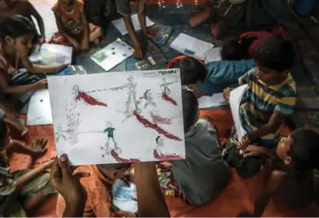  ?? SERGEY PONOMAREV/THE NEW YORK TIMES ?? A Rohingya boy at the Balukhali refugee camp near Cox’s Bazar, Bangladesh, holds up a graphic drawing depicting his experience­s while fleeing Burma.