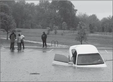 ?? NWA Democrat-Gazette/ANDY SHUPE ?? Residents stand Saturday near a passenger car after it left the pavement and ended up in a drainage area in the middle of a parking area south of the Botanical Garden of the Ozarks in Fayettevil­le.