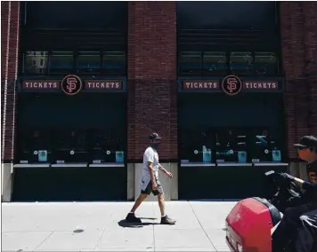  ?? JEFF CHIU — THE ASSOCIATED PRESS ?? A pedestrian and a worker wear masks in front of a ticket office outside of Oracle Park on Thursday. Fans won’t be able to attend Giants games here during the pandemic, but they can submit photos of themselves to be used as fan cutouts.