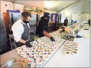  ?? Ted S. Warren / Associated Press ?? Jason Wilson, left, a chef at The Lakehouse, a restaurant located in Bellevue, Wash., and sous chef Demetrius Parker prepare dishes for an outdoor tent set up on the turf at Lumen Field, home of the Seahawks.