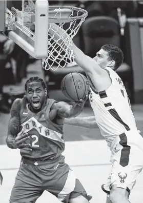  ?? Stacy Revere / Getty Images ?? Raptors star Kawhi Leonard, left, tries to go for two points the hard way, from underneath the rim and arms of the Bucks’ Brook Lopez. Leonard had 35 points.