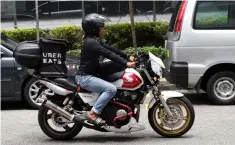  ??  ?? An UBER Eats delivery man rides through the street of Singapore. — AFP photo