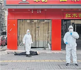  ??  ?? Officials in hazmat suits attend to the body of a man who collapsed and died in a deserted street in Wuhan. The cause of the man’s death was unknown, but police and medical teams were not taking any chances