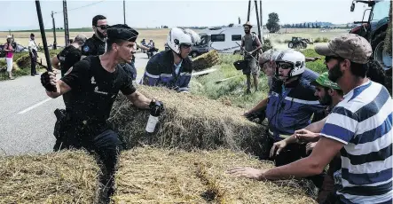  ?? JEFF PACHOUD / AFP / GETTY IMAGES ?? A gendarme holding a baton and tear gas holds back protesters as other gendarmes remove haybales from the Tour de France route during a farmers’ protest Tuesday in the Pyrenees.