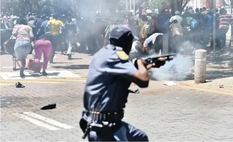  ?? PICTURE: OUPA MOKOENA ?? SCATTER GUN: A police officer fires stun grenades at striking general workers in Hatfield, Pretoria, yesterday during a protest against contract labour by Unisa and the University of Pretoria.