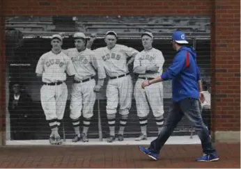  ?? KIICHIRO SATO /THE ASSOCIATED PRESS ?? A fan walks by a photo of old-time Cubs posted on a wall on Waveland Avenue in 2014, when Wrigley turned 100.